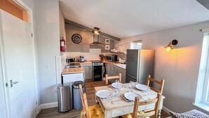 A compact kitchen with a dining area, wooden furniture, and a window providing natural light. - 2 bedroom accommodation in Debenham, near Framlingham (Debenham, near Framlingham)
