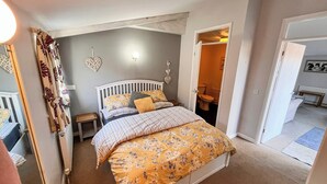 A bedroom with a bed, a nightstand, a wall-mounted light, and a door leading to a bathroom. - 2 bedroom accommodation in Debenham, near Framlingham (Debenham, near Framlingham)