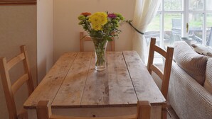 A wooden dining table with a vase of flowers, surrounded by wooden chairs, in a room with a window and a view of the outdoors. - 2 bedroom accommodation in Debenham, near Framlingham (Debenham, near Framlingham)