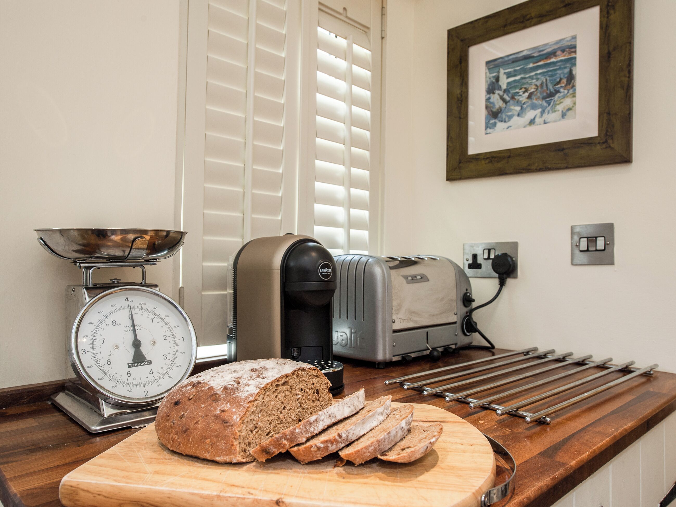 A kitchen with a loaf of bread, a bread slicer, a scale, and a toaster.