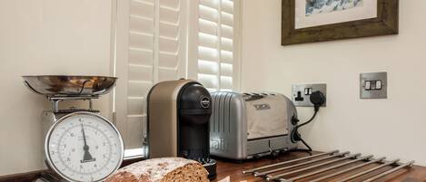 A kitchen with a loaf of bread, a bread slicer, a scale, and a toaster.