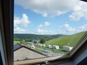 A view through a window of a campsite with RVs, a lake, and rolling hills. - The Cob Barn - UKC1852 (Shaldon, near Teignmouth)