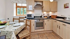 Una cocina con armarios de madera, microondas, horno, pileta y una mesa de comedor preparada para dos personas.
