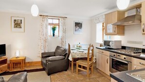 Un espacio habitable compacto con kitchenette, comedor con mesa y sillas, sofá y televisor.