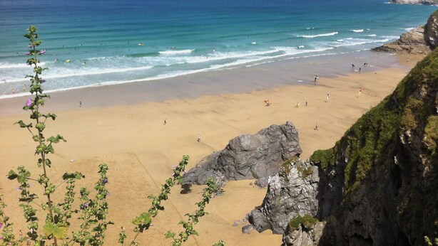 Uma praia com águas azuis cristalinas, areal arenoso e afloramentos rochosos.