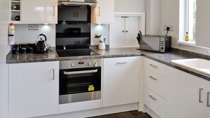 Uma cozinha moderna com armários brancos, forno embutido, fogão e uma janela que oferece luz natural.