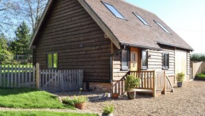 A wooden cabin with a sloped roof, a front porch, and a gravel driveway. - 3 bedroom accommodation in Ninfield, near Battle (Ninfield, near Battle)