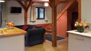 A cozy living room with a sofa, a wooden staircase, and a kitchen area with a fruit bowl and a vase of flowers. - 3 bedroom accommodation in Ninfield, near Battle (Ninfield, near Battle)