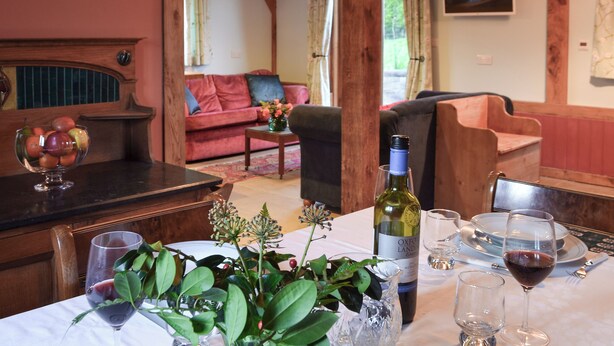 A dining area with a table set for a meal, a bottle of wine, and a glass of red wine. - 3 bedroom accommodation in Ninfield, near Battle (Ninfield, near Battle)