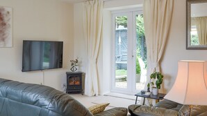A living room with a sofa, a television, a fireplace, a table with a lamp, and a sliding glass door leading to an outdoor area. - 1 bedroom accommodation in Gunville, near Newport (Gunville, near Newport)