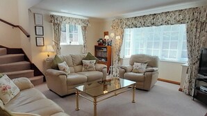 Ein Wohnzimmer mit einer Sofagarnitur, einem Couchtisch, einem Bücherregal und einem Fernseher.