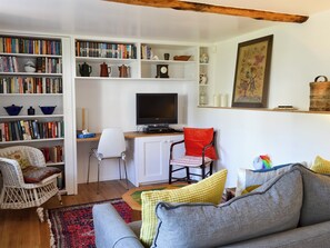 A cozy living room with a bookshelf, a television, a red chair, a grey sofa, and a patterned rug.
