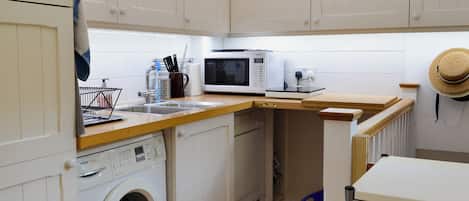 Una cocina compacta con lavadora, microondas y lavabo.