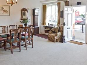 Ein gemütliches Wohnzimmer mit Esstisch, Stühlen, einem floralen Sessel, einem großen Spiegel und einem Bücherregal.