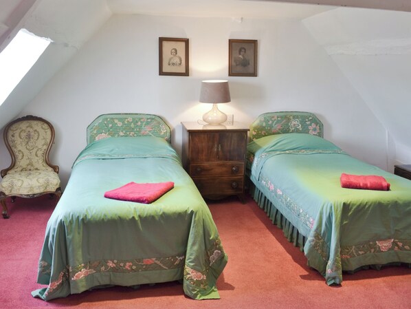A bedroom with two twin beds, a wooden nightstand, a chair, and two framed pictures on the wall.
