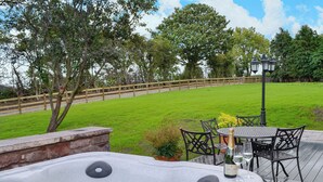 Un jacuzzi con borde de piedra, mesa y sillas al aire libre, y una terraza de madera.