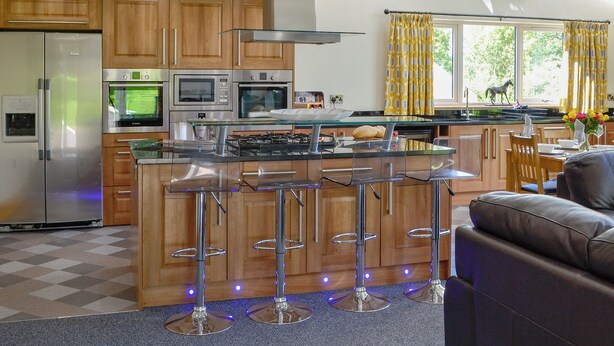 Una cocina moderna con electrodomésticos de acero inoxidable, armarios de madera y una isla central con taburetes de bar.