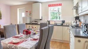 A dining area with a table set for four, a kitchen with white cabinets, and a window with a view of greenery. - 3 bedroom accommodation in Great Hatfield, near Hornsea (Great Hatfield, near Hornsea)