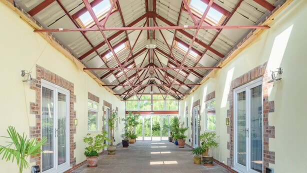 A covered corridor with potted plants, a tiled floor, and a high ceiling with metal beams. - 3 bedroom accommodation in Great Hatfield, near Hornsea (Great Hatfield, near Hornsea)