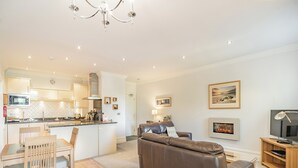 A modern living room with a leather sofa, a dining area with a wooden table and chairs, a kitchen with white cabinets, and a fireplace. - Apartment 14, Hazelwood Hall (Silverdale, near Arnside)