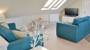 A modern living room with a teal sofa, a white coffee table, and a decorative tree. There are skylights, a TV, and a radiator. - Swift Cottage - UKC3435 (East Ogwell, near Newton Abbot)