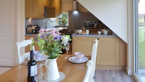 A modern kitchen with wooden cabinets, a dining table set with white plates, glasses, and a vase of flowers. - Swift Cottage - UKC3435 (East Ogwell, near Newton Abbot)