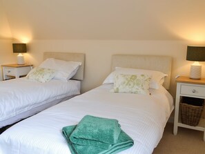 Two twin beds with white bedding and green floral pillows, bedside tables with lamps, and a wicker basket on one table. - The Old Gasworks Building (Montrose)