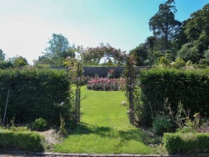 Ein Garten mit einem zentralen Torbogen, umgeben von üppiger Vegetation und blühenden Pflanzen.
