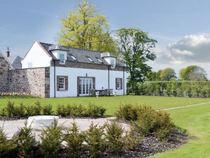 A white building with a stone facade, a lawn, and a large tree.