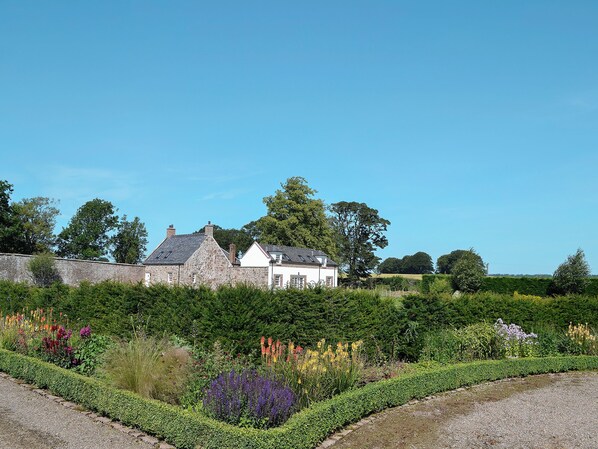 A stone house with a white exterior, surrounded by a well-maintained garden with various plants and flowers.