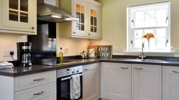 A kitchen with white cabinets, a stove, an oven, a coffee maker, and a window with a flower vase.
