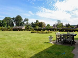 A well-maintained lawn with a wooden bench and table, surrounded by neatly trimmed hedges and a variety of plants.