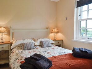 A bedroom with a bed, two bedside tables with lamps, a window with a view, and a neatly made bed with towels.