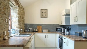 A kitchen with white cabinets, a wooden countertop, a stone wall, and a microwave.