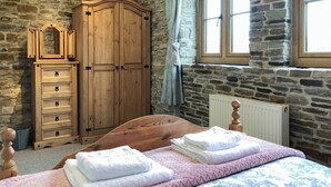 A bedroom with a stone wall, a wooden wardrobe, a bed with pink bedding, and a window with curtains.