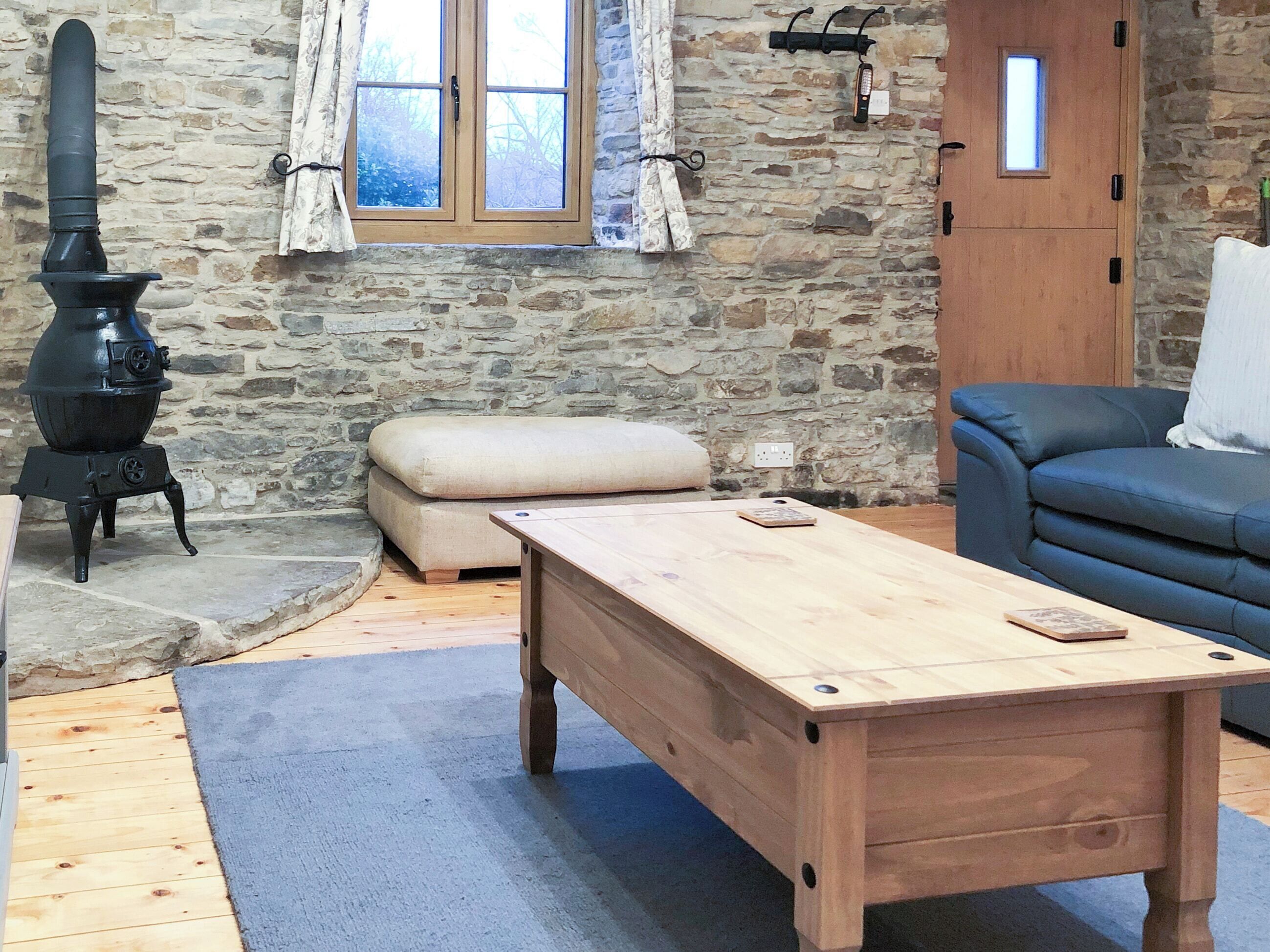 A rustic room with a stone wall, a wooden table, a blue sofa, and a black stove.