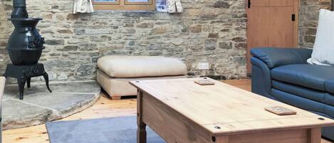 A rustic room with a stone wall, a wooden table, a blue sofa, and a black stove.