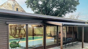 A covered patio area with a glass enclosure overlooking a swimming pool.