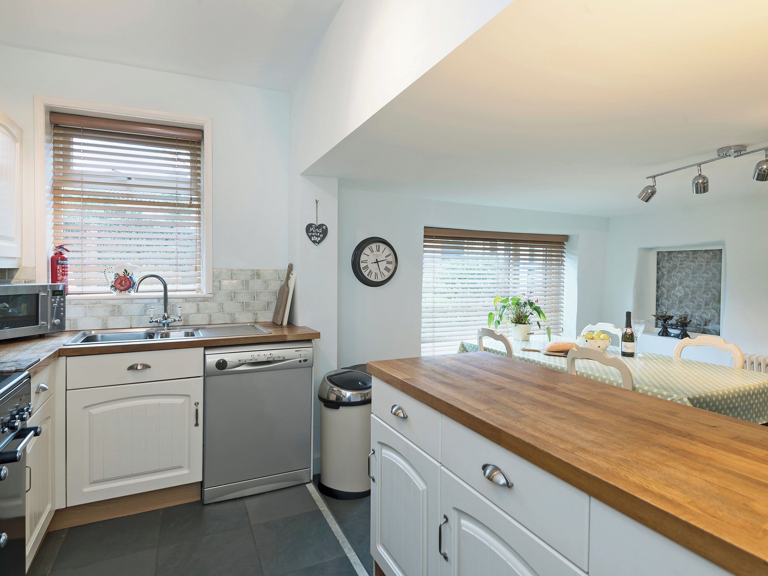A compact kitchen with white cabinetry, a wooden countertop, a dishwasher, and a trash bin.