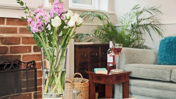 A living room with a glass table, a vase with flowers, a fireplace, a sofa, and a wine bottle. - Horseshoe House - UKC2743 (Saham Toney, near Thetford)