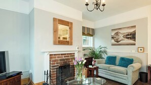 A living room with a fireplace, a sofa, a glass coffee table, and a television. - Horseshoe House - UKC2743 (Saham Toney, near Thetford)
