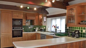 A kitchen with wooden cabinets, a microwave, an oven, a dishwasher, and a window with curtains.