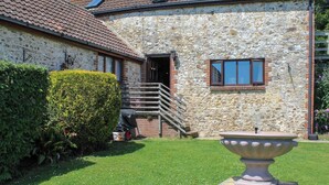 A stone building with a tiled roof, a wooden staircase, and a garden with a large urn.