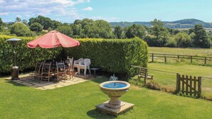 A patio with a table and chairs, a red umbrella, and a fountain.