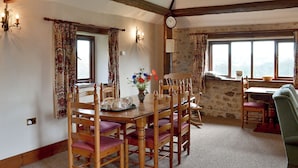 A dining area with a wooden table and chairs, a clock on the wall, and a ceiling fan.