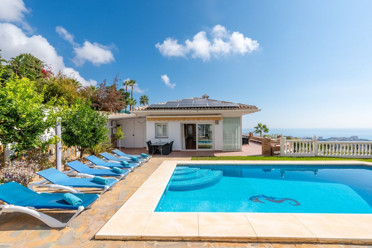 A pool area with lounge chairs, a building with a view, and a clear sky.