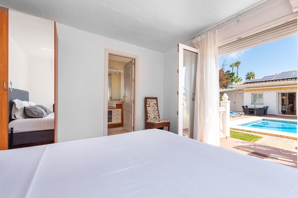 A bedroom with a large bed, a wardrobe, a chair, and a view of an outdoor swimming pool.