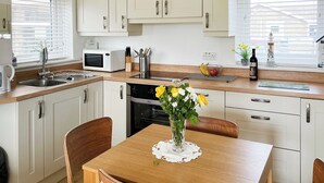 A modern kitchen with white cabinets, a microwave, a sink, and a dining area with a wooden table and chairs. - 2 bedroom accommodation in Beadnell (Beadnell)
