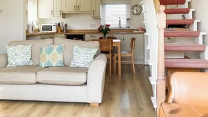 A living room with a sofa, a coffee table, and a staircase. - 2 bedroom accommodation in Beadnell (Beadnell)
