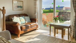 A living room with a brown leather sofa, a wooden coffee table, and a patterned rug. - 2 bedroom accommodation in Beadnell (Beadnell)